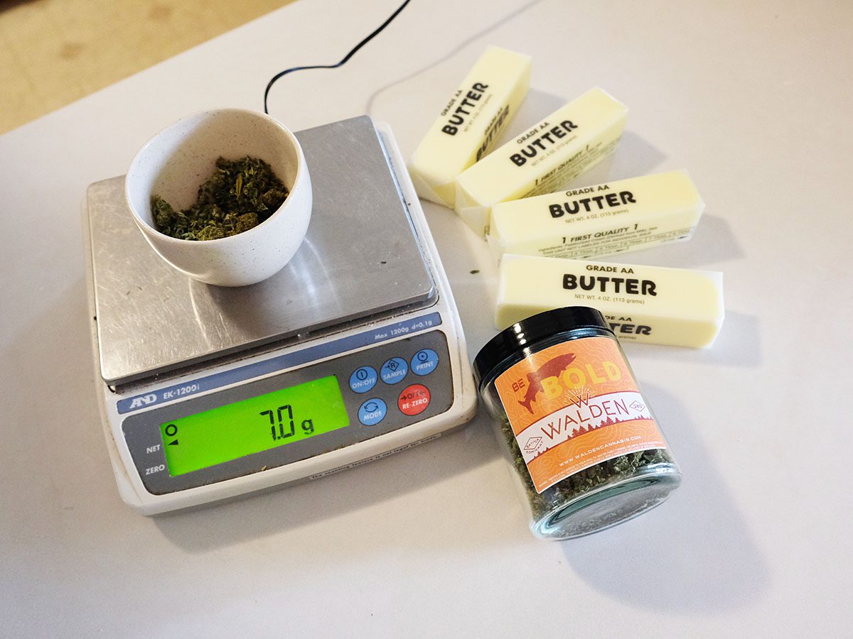 A scale showing cannabis weighed out to 7 grams. 4 sticks of butter are next to the scale.