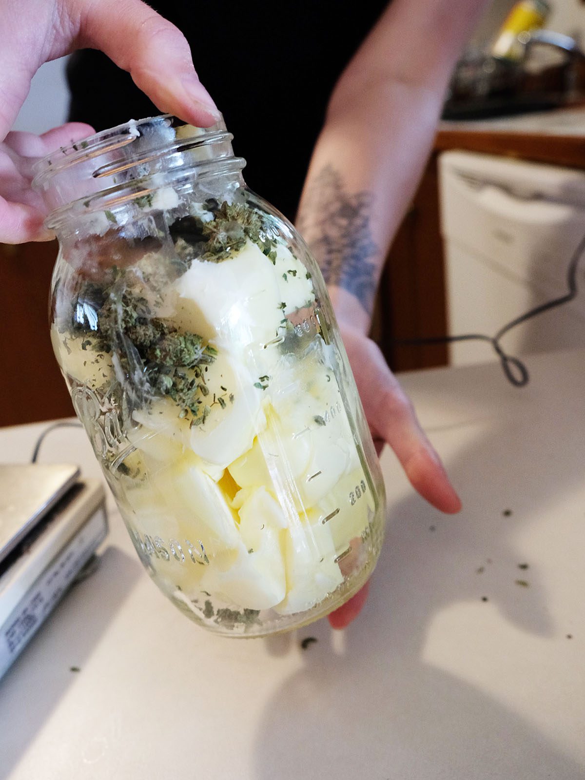 hands holding a mason jar of butter and ground cannabis